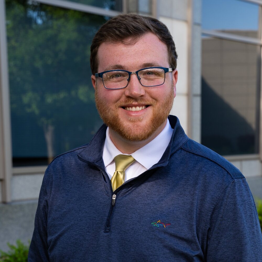 Matthew Smith smiling in a navy quarter-zip and gold tie