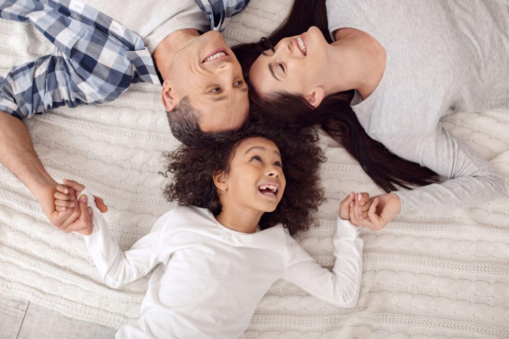 A family of three laying on a bed together, smiling and hugging each other warmly