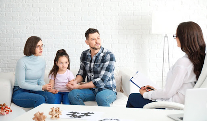 A family sitting on a couch in front of a therapist, engaged in family counseling.