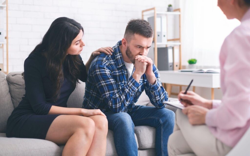 Couple on couch, man writing on paper.