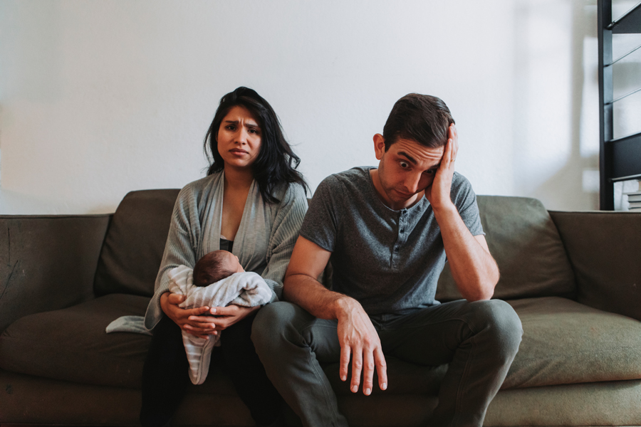 A couple sits on a couch, embracing their newborn baby, capturing a serene and intimate family moment.